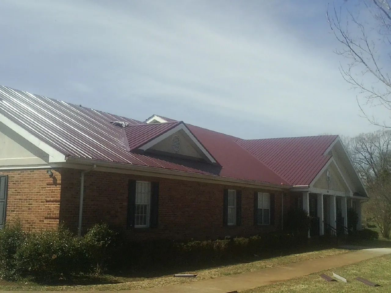 Red metal roof with gabled entries on a long brick building, from a Hail Damage Roof Repair job in East Templeton