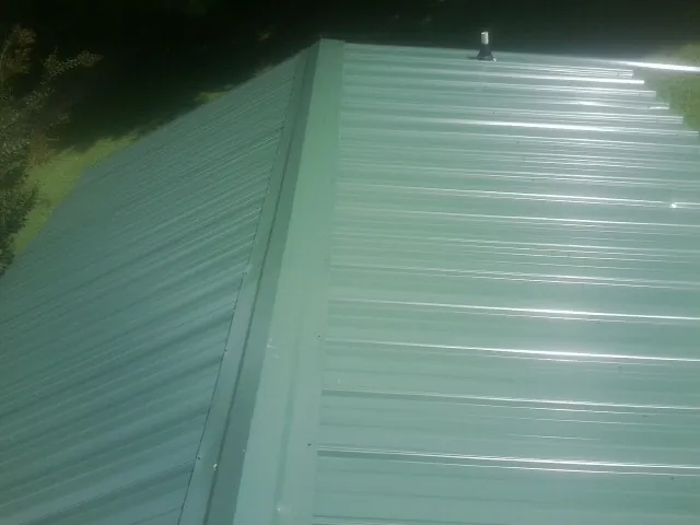New green metal panels meeting at the ridge of a roof — Flat Roof Repair work by our crew in East Templeton
