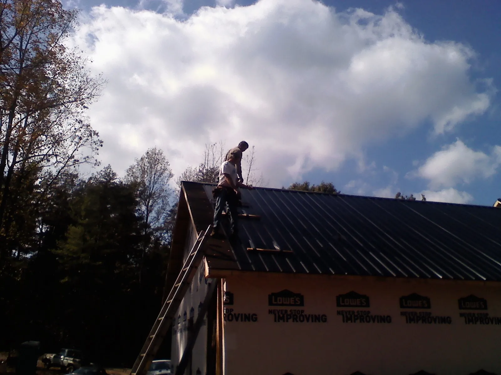 Roofer fastening dark metal panels high against a cloudy sky, from a Roof Inspection job in East Templeton