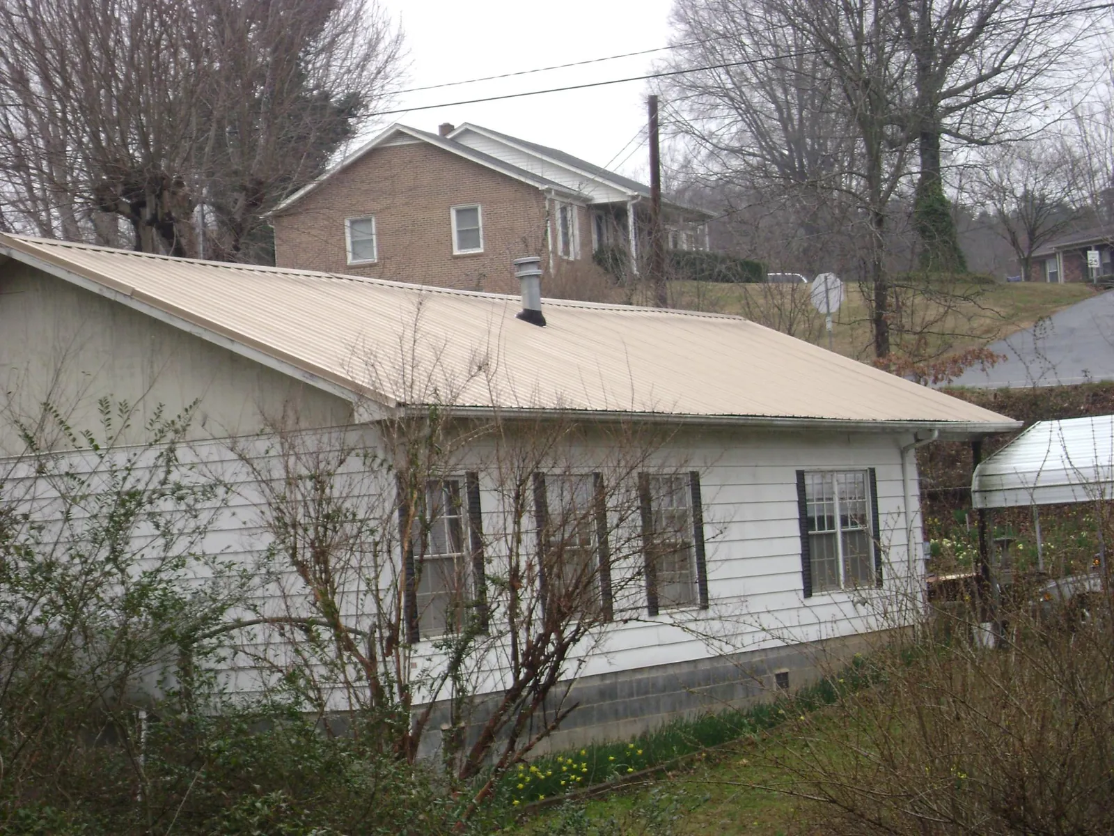 Tan metal roof on a white sided house set into a hillside — Commercial Roofing by Roofing Brothers in East Templeton